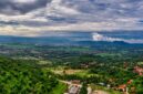 Wisatawan menikmati pemandangan hijau pegunungan Indonesia dari balik jendela lebar kereta api eksekutif yang nyaman.