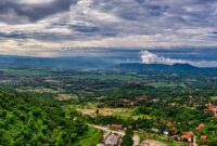 Wisatawan menikmati pemandangan hijau pegunungan Indonesia dari balik jendela lebar kereta api eksekutif yang nyaman.