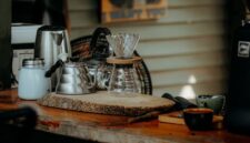 Seorang warga Desa Adat Kemiren menyeduh kopi tradisional menggunakan cangkir tanah liat di tengah suasana pedesaan Banyuwangi yang asri.