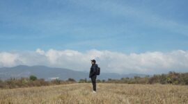 Seorang pelancong yang membawa tas punggung ringkas berjalan santai di area terminal keberangkatan bandara tanpa terbebani oleh koper berukuran besar.