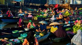 Seorang pelancong menikmati suasana tenang pedesaan di Flores sembari berinteraksi dengan warga lokal yang sedang mengolah kain tenun tradisional.
