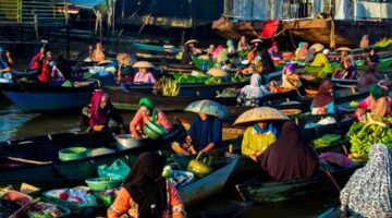 Seorang pelancong menikmati suasana tenang pedesaan di Flores sembari berinteraksi dengan warga lokal yang sedang mengolah kain tenun tradisional.