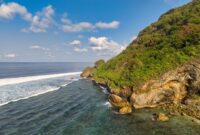 Pemandangan bukit hijau berlapis pantai perawan di wilayah kepulauan terpencil Indonesia yang menawarkan pengalaman wisata tenang jauh dari hiruk-pikuk perkotaan.
