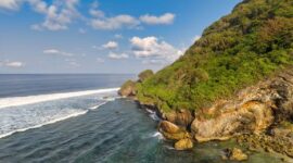 Pemandangan bukit hijau berlapis pantai perawan di wilayah kepulauan terpencil Indonesia yang menawarkan pengalaman wisata tenang jauh dari hiruk-pikuk perkotaan.