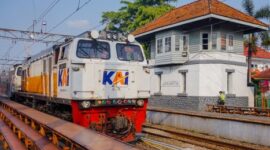 Penumpang menikmati pemandangan perbukitan hijau dari dalam gerbong kereta api pariwisata yang nyaman. Transportasi rel kini menjadi favorit pelancong yang menginginkan perjalanan santai tanpa terkendala kemacetan jalan raya.