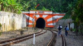 Wisatawan menikmati pemandangan perbukitan hijau dan persawahan dari balik jendela kaca lebar gerbong kereta wisata.