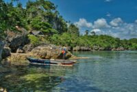 Perahu kayu tradisional melintas di atas perairan jernih Kepulauan Alor yang memperlihatkan keindahan bawah laut alami tanpa tercemar.