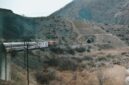 Pemandangan jalur kereta api yang membelah kawasan perbukitan hijau, menawarkan pengalaman perjalanan lambat yang sarat akan ketenangan visual bagi para pelancong.