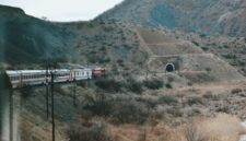 Pemandangan jalur kereta api yang membelah kawasan perbukitan hijau, menawarkan pengalaman perjalanan lambat yang sarat akan ketenangan visual bagi para pelancong.